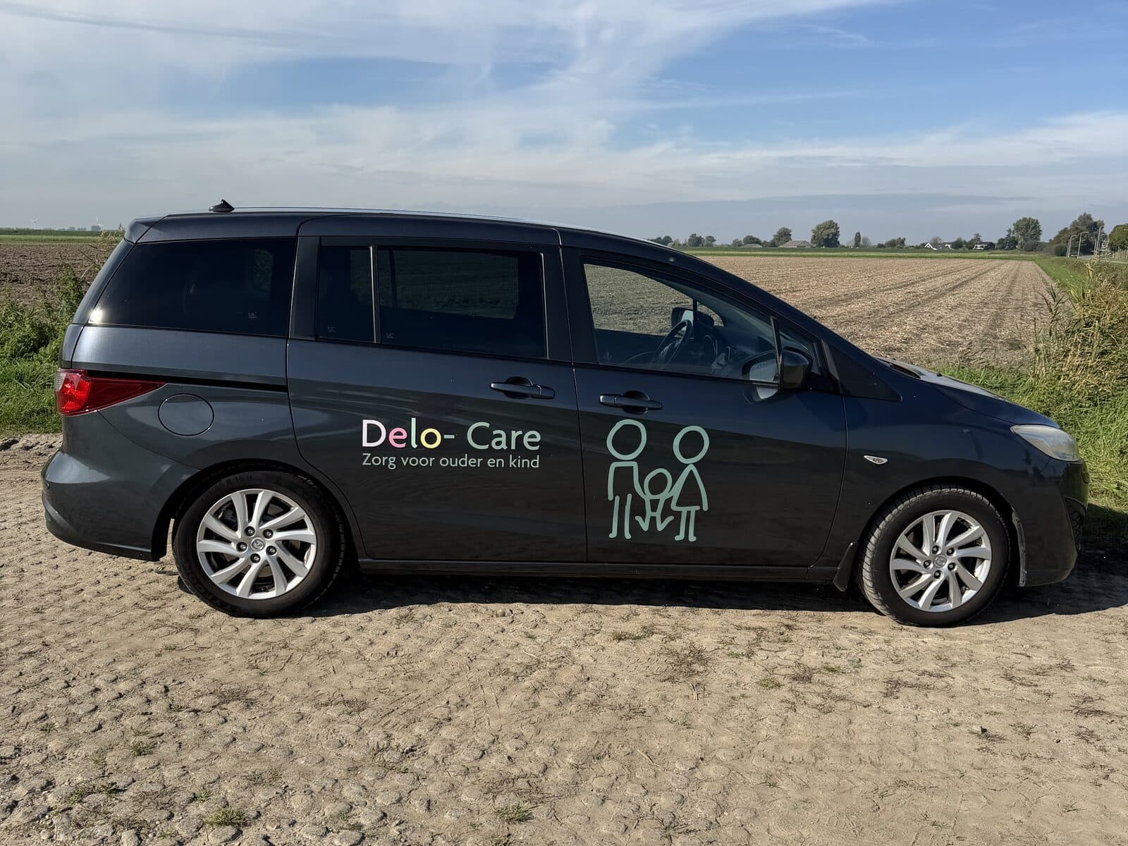 Onze zevenpersoonsauto met het Delo-Care-logo op de zijkant