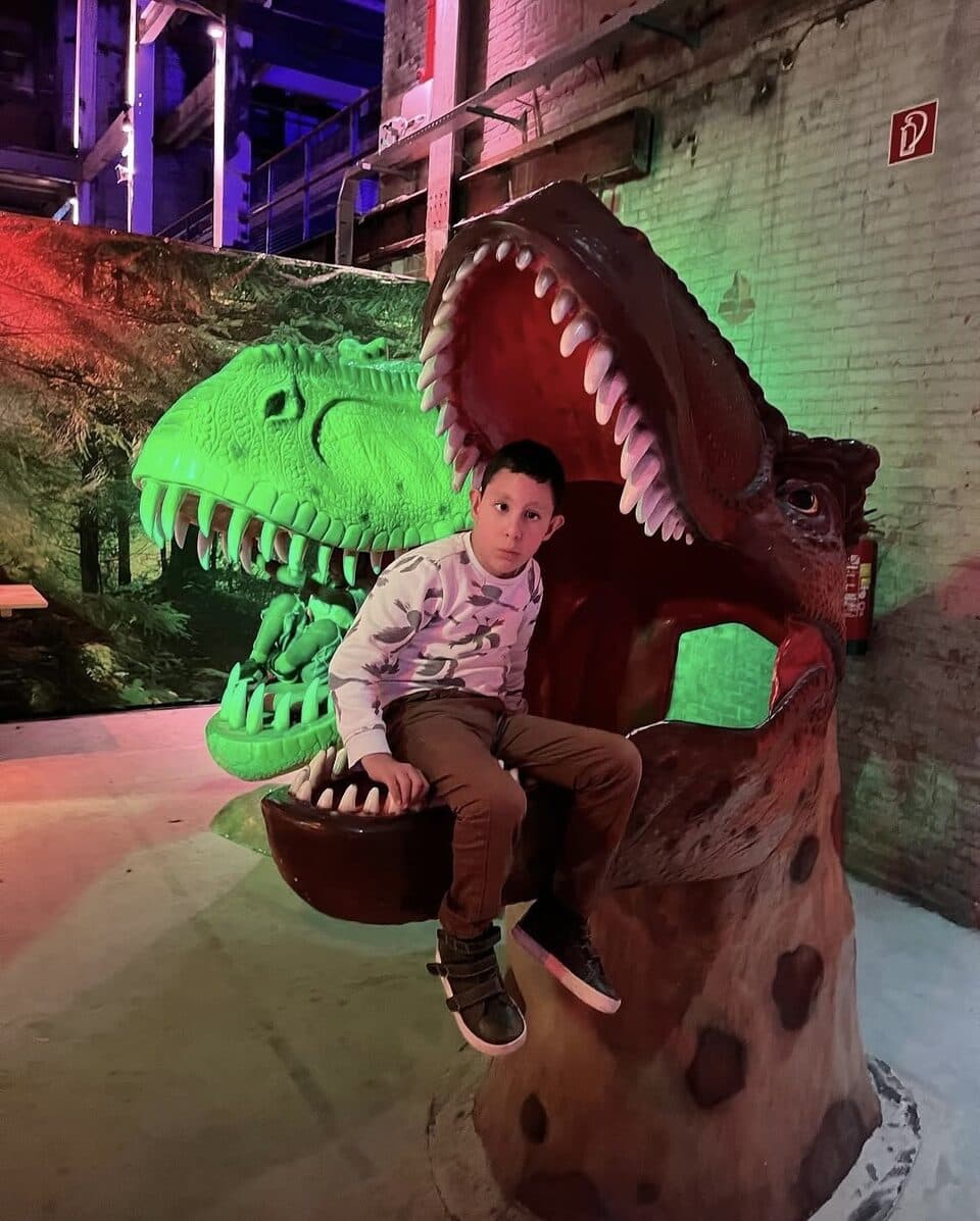 Een kind zit in de bek van een dinosaurusbeeld